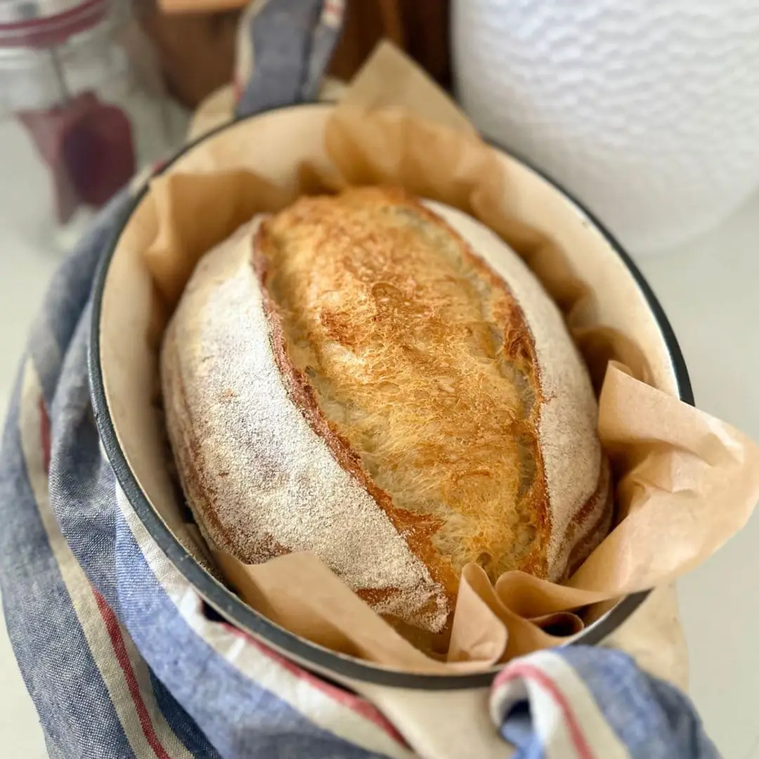 Freshly baked loaf of sourdough bread in a blue ceramic bowl, symbolizing the simple art of cultivating joy at home.